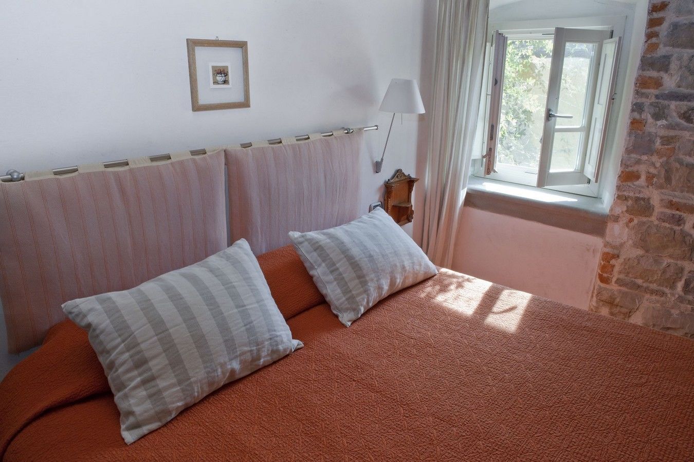 Ein Schlafzimmer mit Bett, zwei Kissen, einem Nachttisch, einer Lampe, einem Bild an der Wand und einem Fenster mit Vorhängen.