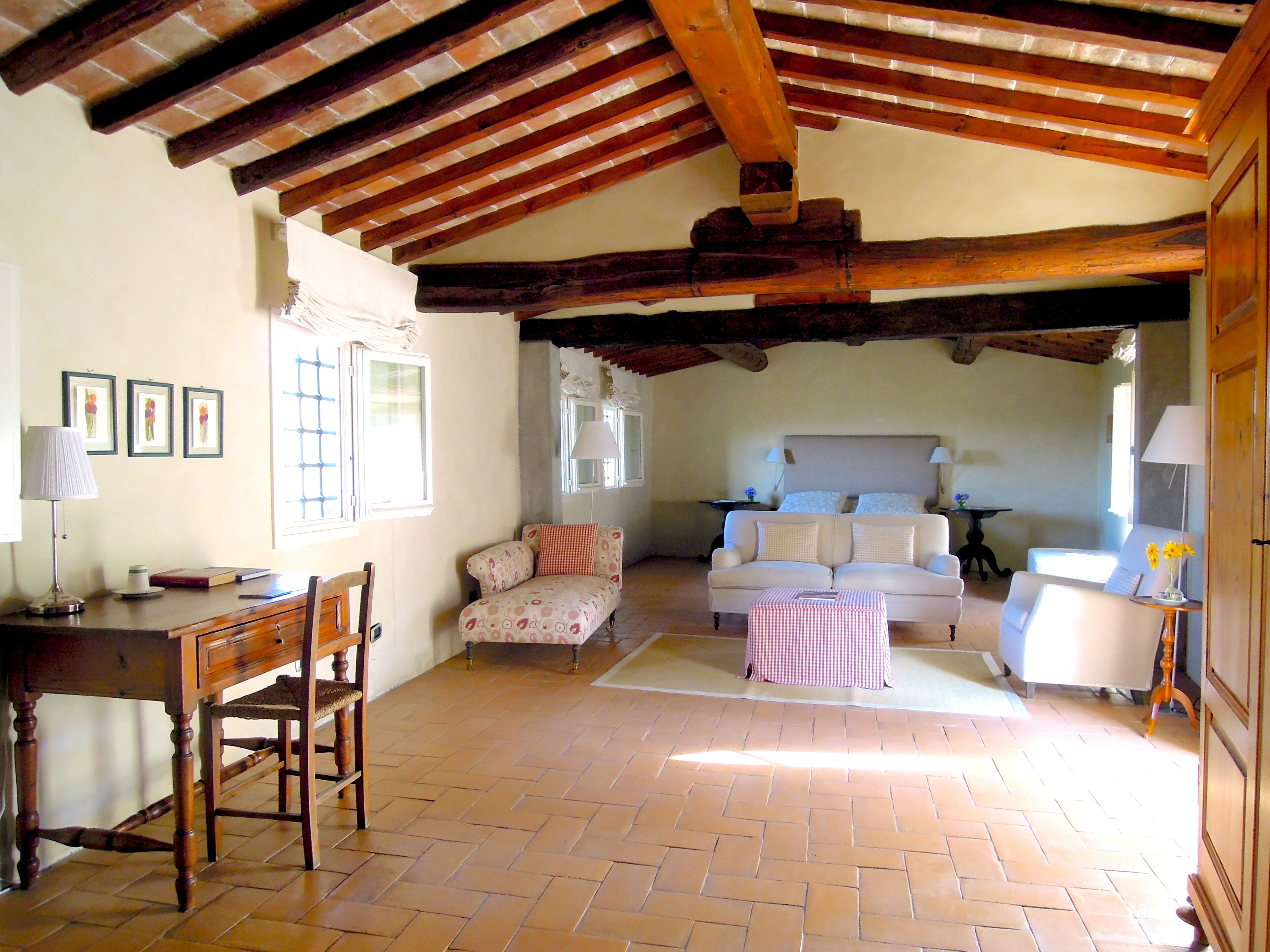 Una habitación acogedora con techo de madera, una cama con almohadas, una mesita, una silla y una lámpara.