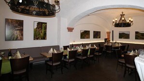 A restaurant with multiple tables and chairs, a chandelier, and framed artwork on the walls. - Weingut Gästehaus Derkum (Uerzig)