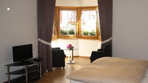 A hotel room with a bed, a TV, a small table with a flower, and a window with curtains. - Weingut Gästehaus Derkum (Uerzig)