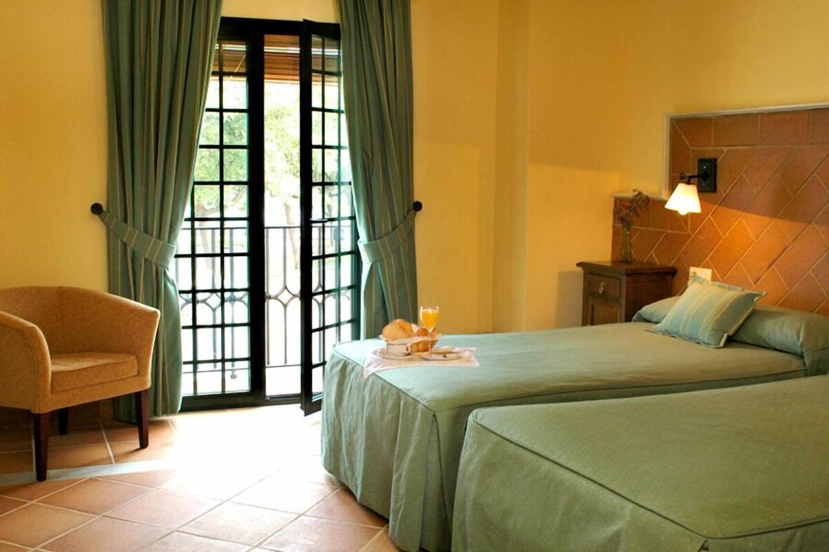 Une chambre avec deux lits, une chaise, une table de chevet et une fenêtre avec des rideaux.