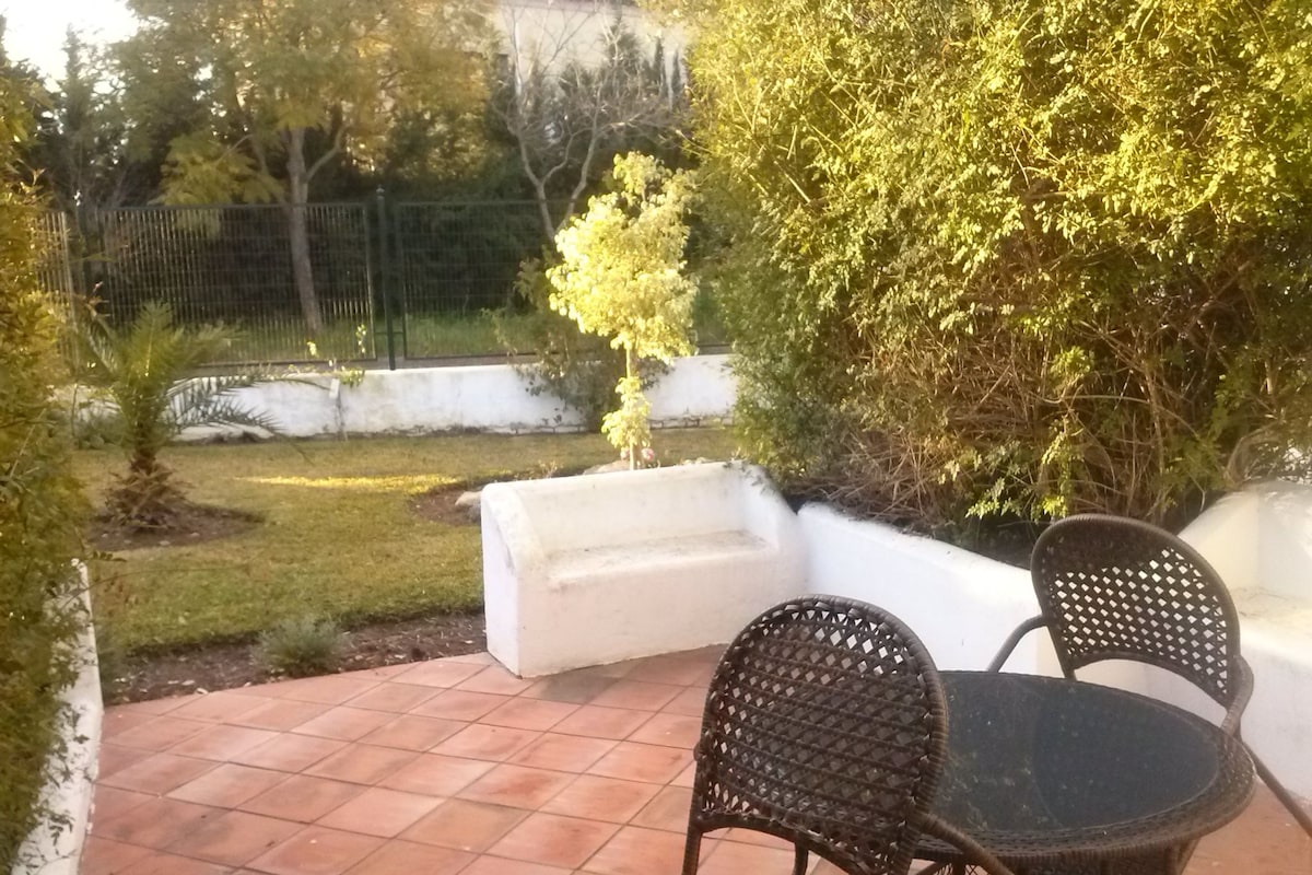 Een terras buiten met betegelde vloer, een witte bank en rieten stoelen.