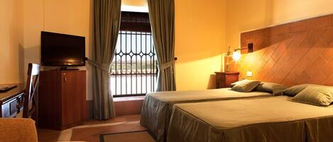 A hotel room with a bed, a TV, a desk, and a window with curtains.
