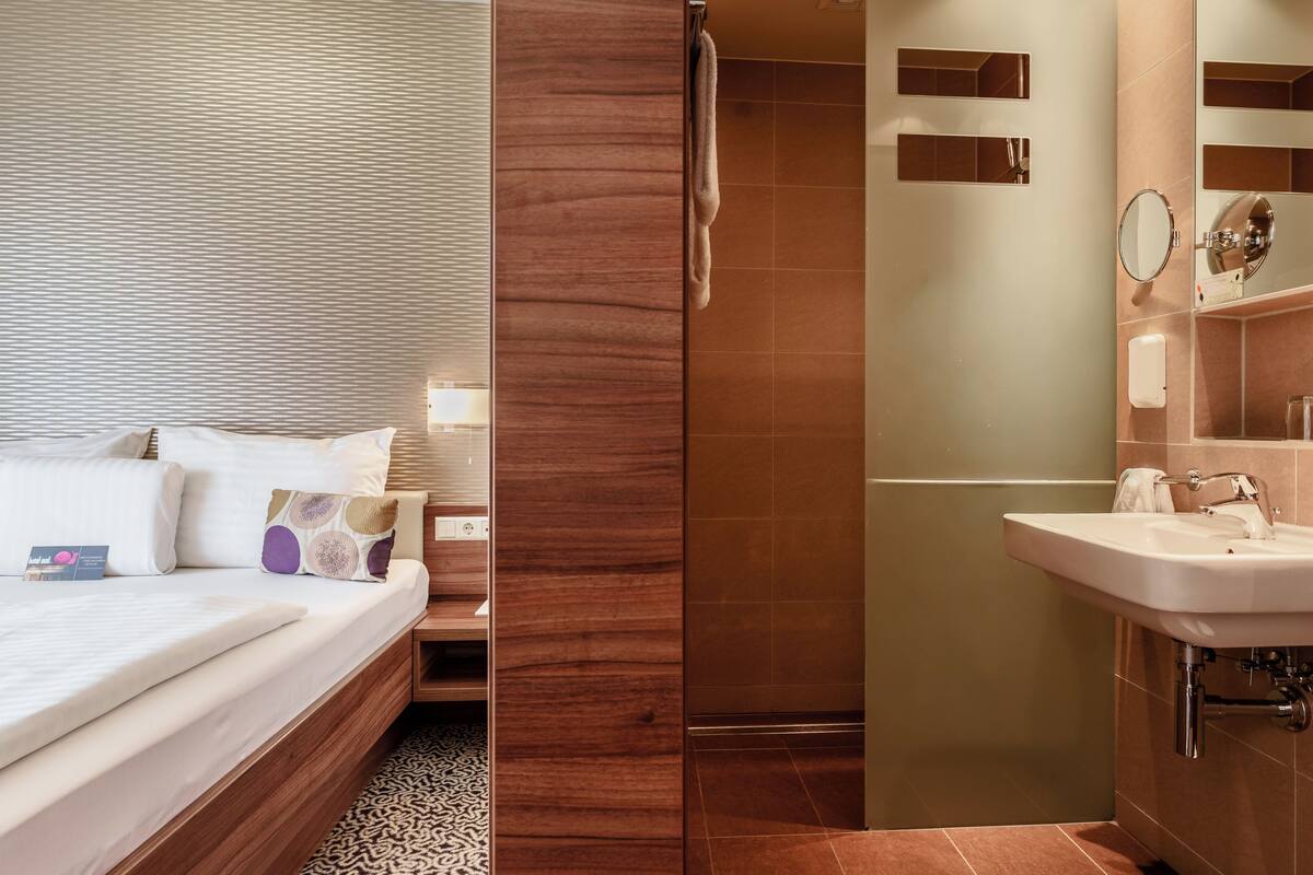 A hotel room with a bed, bedside table, and a bathroom with a sink and mirror.