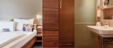 Habitación de hotel con cama, mesita de noche y baño con lavamanos y espejo.