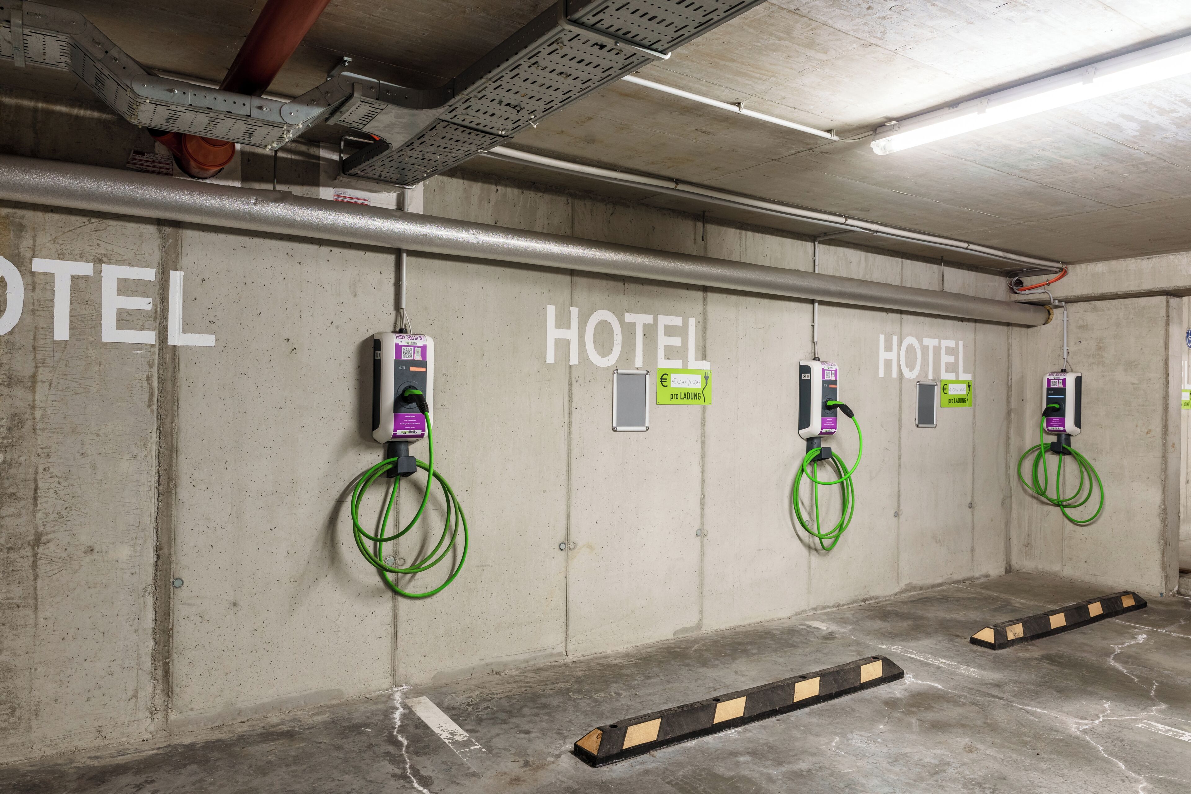Un garaje de hotel para estacionamiento con múltiples estaciones de carga para vehículos eléctricos, paredes de concreto y un diseño industrial y limpio.