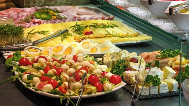 Een buffet met diverse soorten eten, waaronder salades, kazen en gebak.