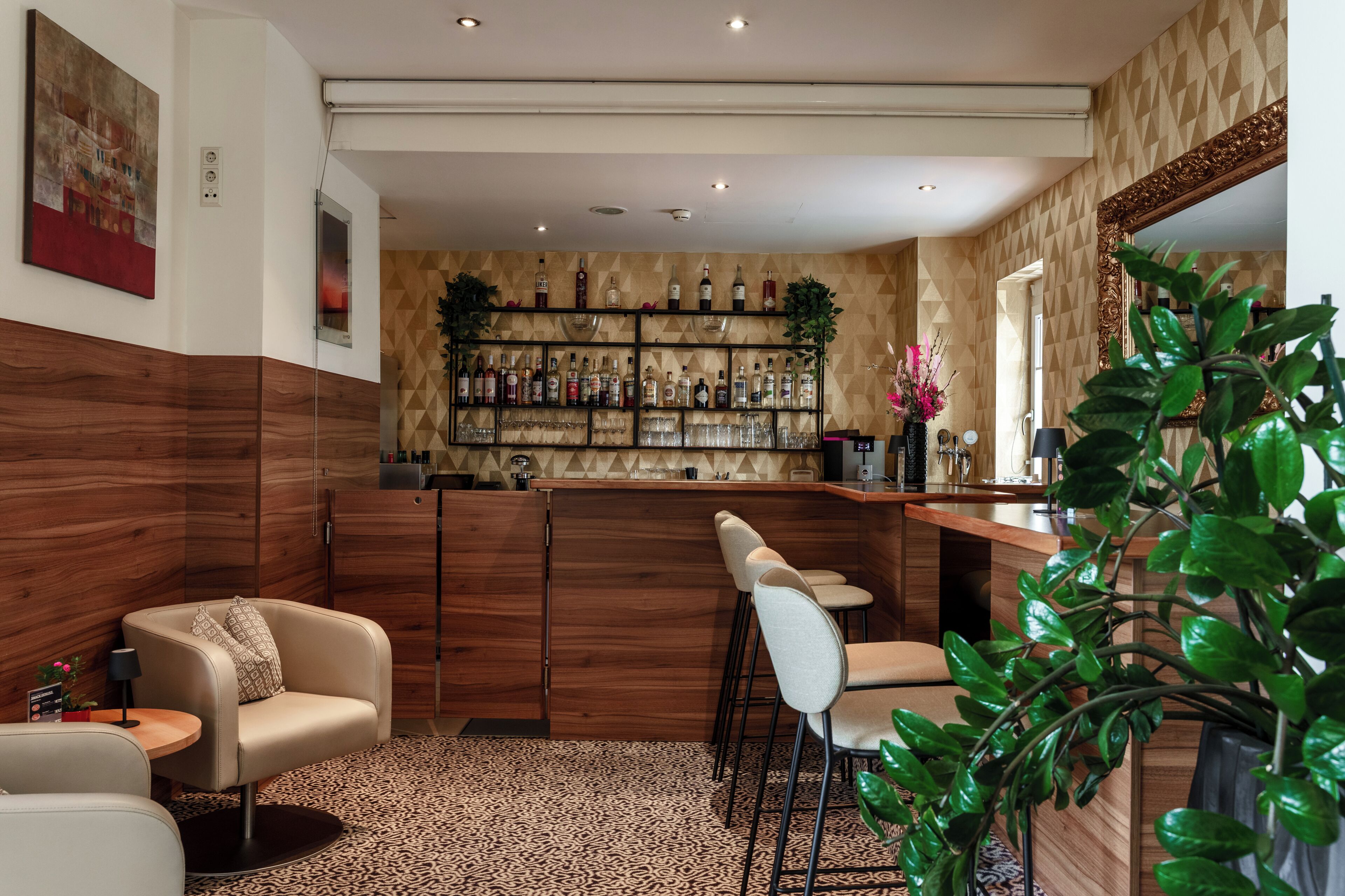 A bar area with a wooden bar counter, multiple stools, and a wall of liquor bottles.