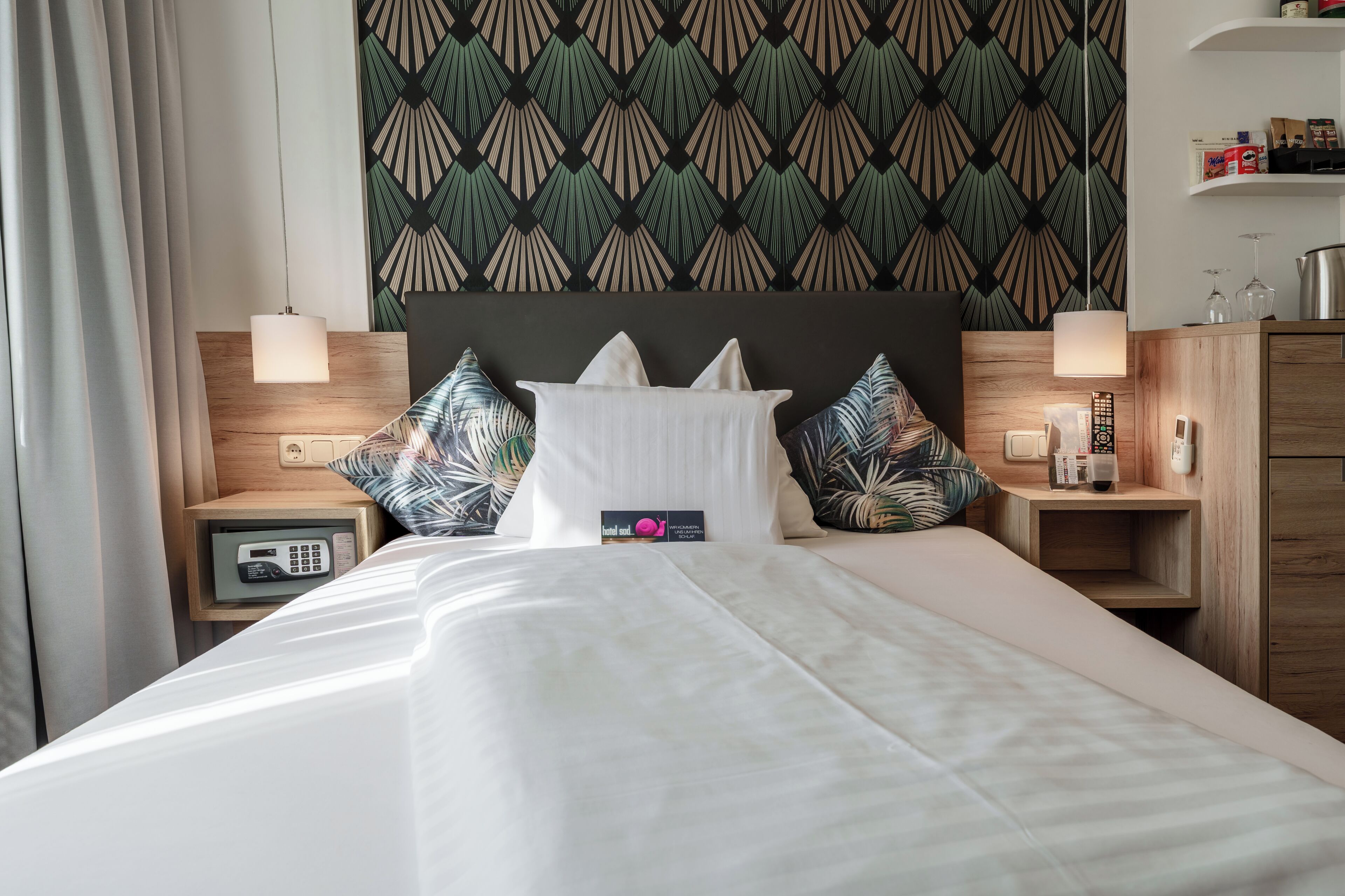 A hotel room with a bed, nightstands, a wooden headboard, and a patterned wallpaper.