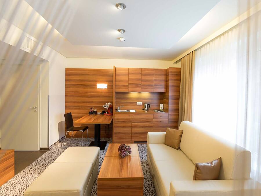 Una moderna camera d'albergo con angolo cottura in legno, un divano, un tavolino da caffè e un'area pranzo.