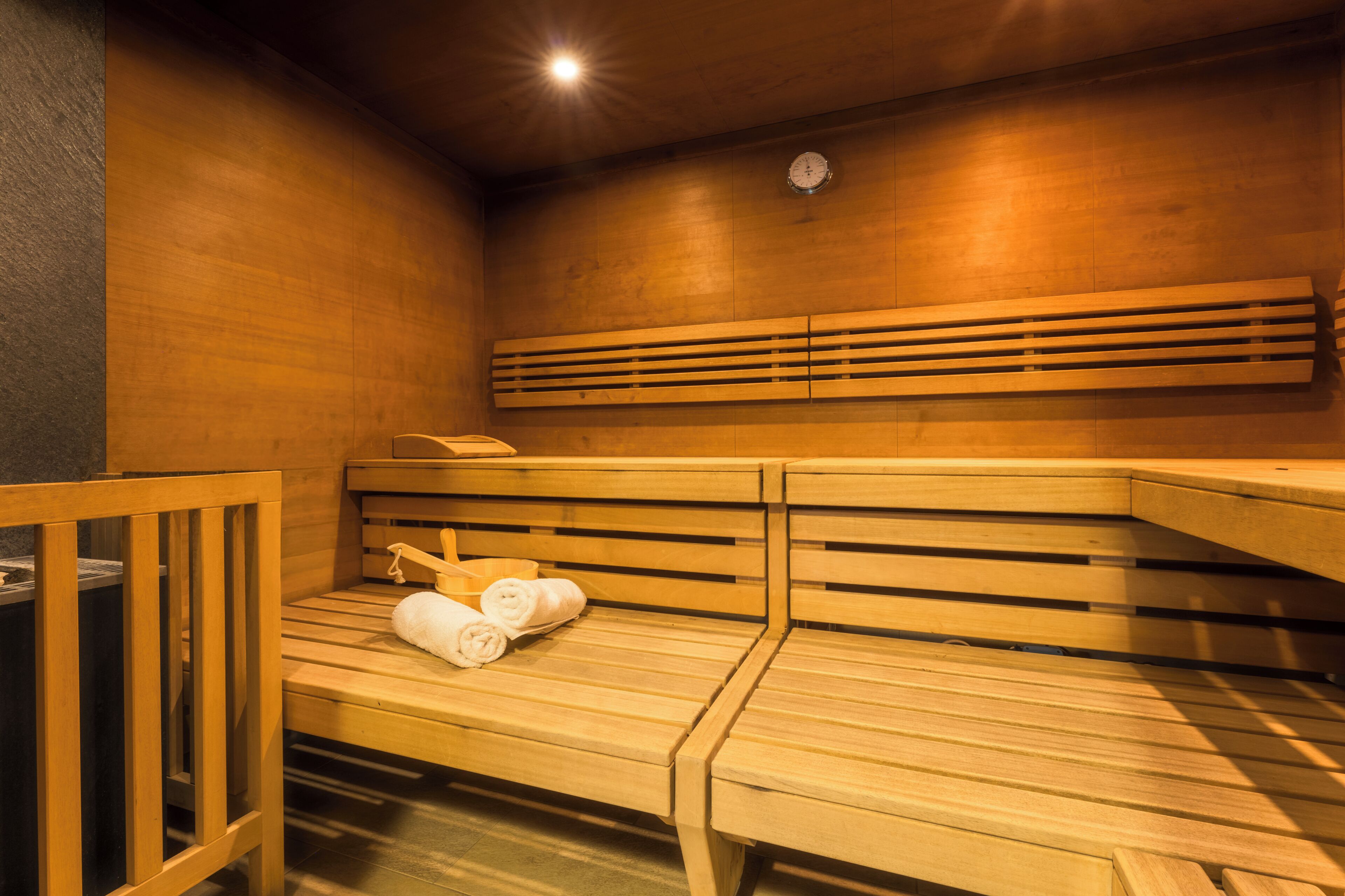 A sauna room with wooden benches, a clock on the wall, and towels on one bench.