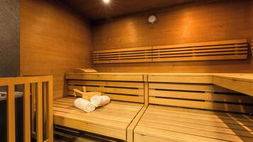 A sauna room with wooden benches, a clock on the wall, and towels on one bench.