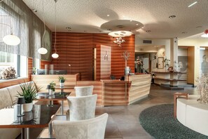 A modern hotel lobby with a reception desk, seating area, and a large mirror. - Hotel Süd art (Graz)