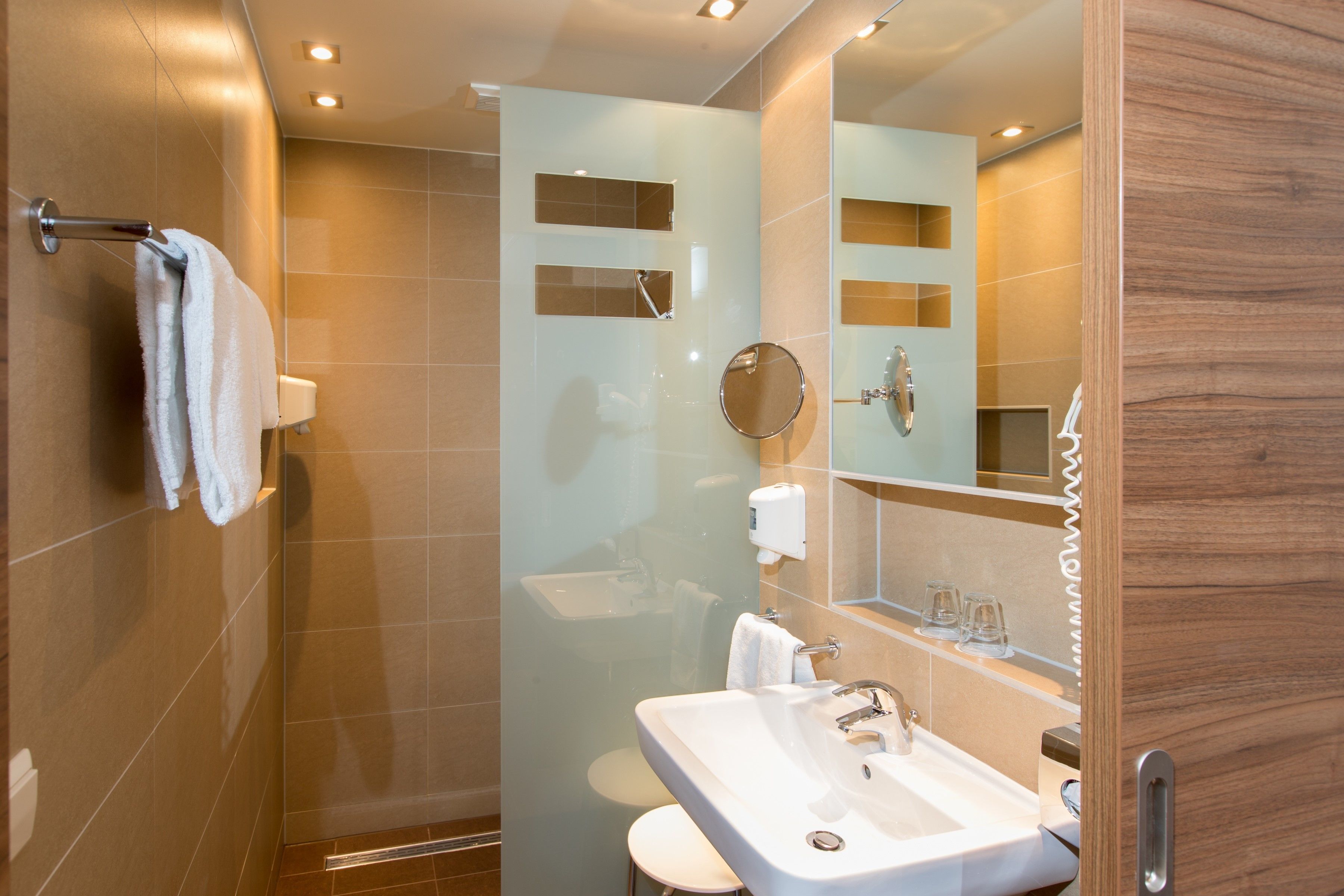 A modern bathroom with a glass-enclosed shower, a sink with a mirror, and a towel rack.