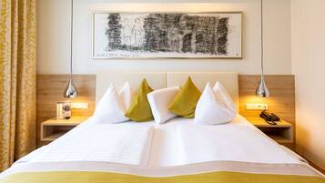 Habitación de hotel con una cama grande, una mesita de noche con lámpara, un teléfono y una obra de arte enmarcada en la pared.