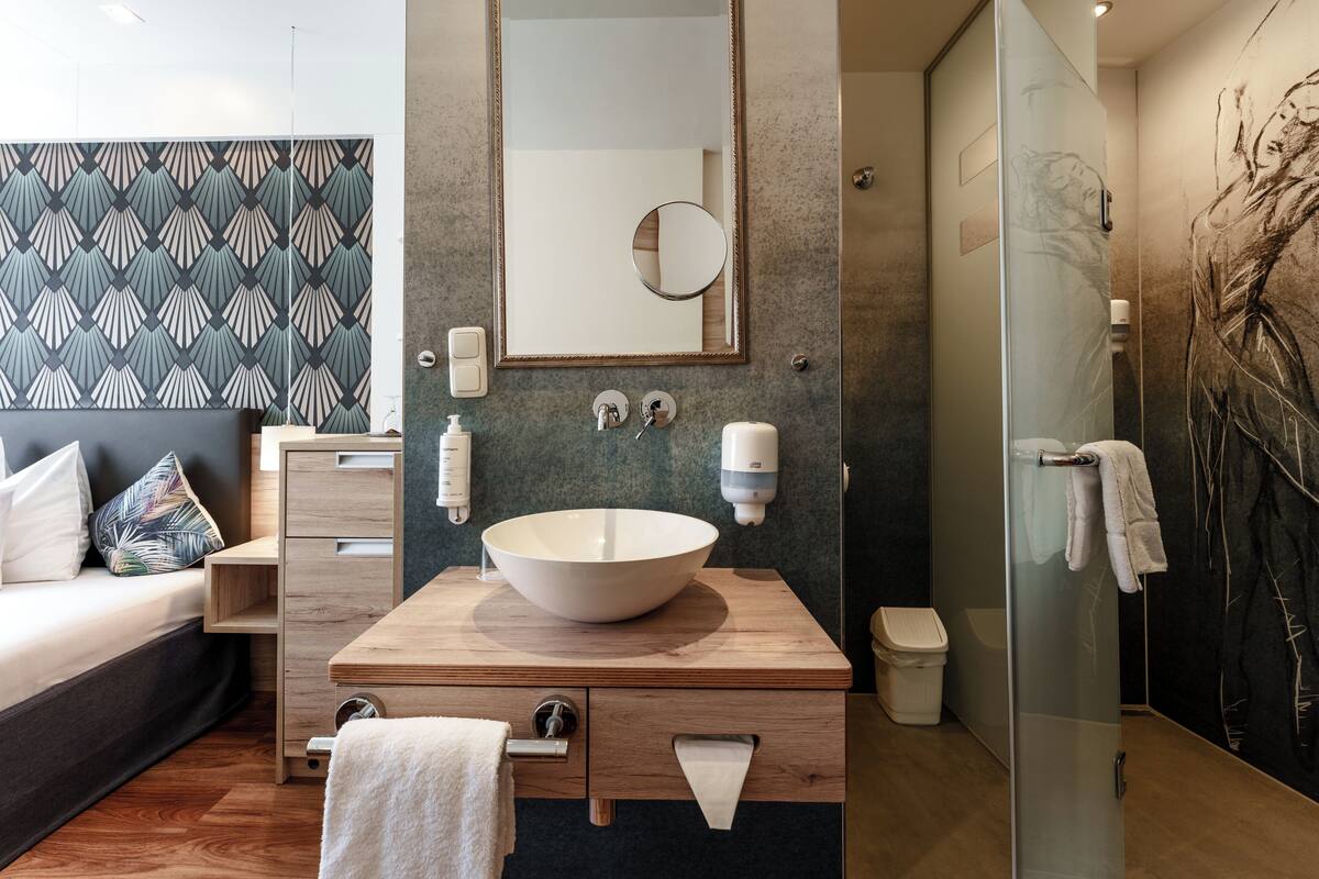 A modern bathroom with a large mirror, a vessel sink, a towel rack, and a glass shower enclosure.