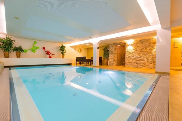An indoor swimming pool with clear water, surrounded by a modern interior with stone walls and potted plants. - Hotel Süd art (Graz)