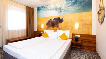Ein Hotelzimmer mit einem großen Bett, einem Holzkopfstück, zwei Nachttischen, einem Wandbild von einem Nashorn und einem Fenster mit Vorhängen.