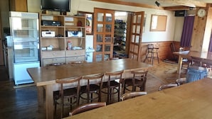 A wooden dining area with a large table and chairs, a refrigerator, and a television on a shelf. - Rental Lodge WHITE RABBIT Madarao kogen Cottage RABBIT (Iiyama)