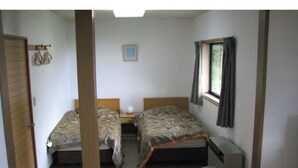 A small, simple room with two beds, a window with curtains, and a small table with a lamp. - Rental Lodge WHITE RABBIT Madarao kogen Cottage RABBIT (Iiyama)