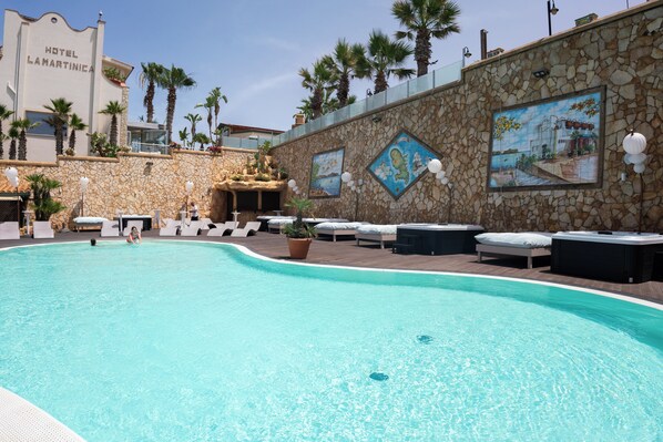 A swimming pool with lounge chairs and a stone wall with paintings.