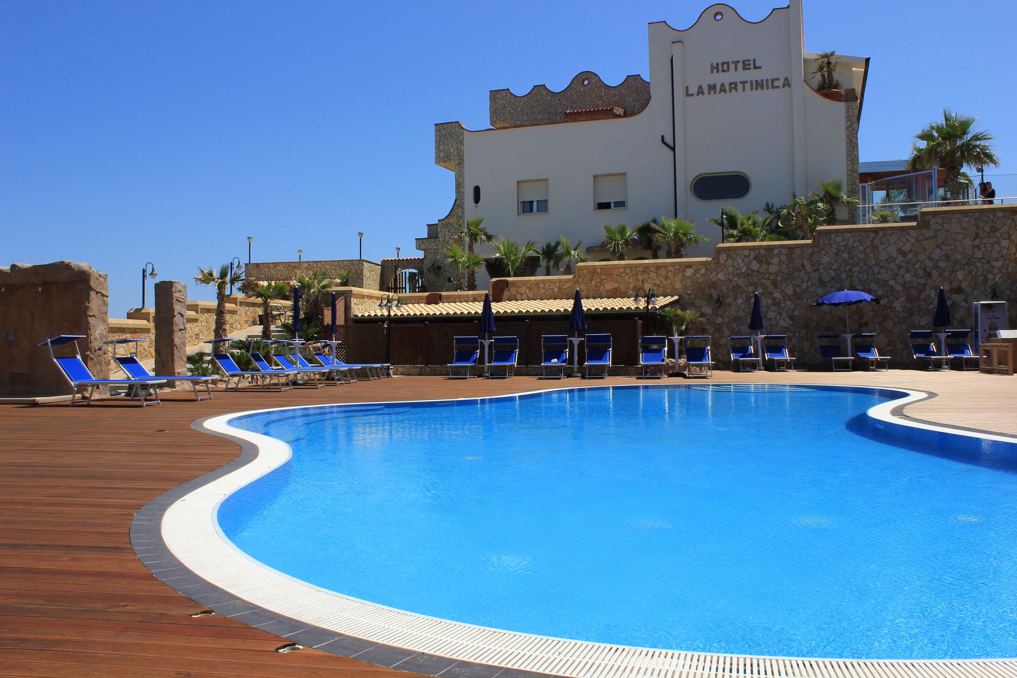 A hotel pool area with blue lounge chairs and a stone wall.