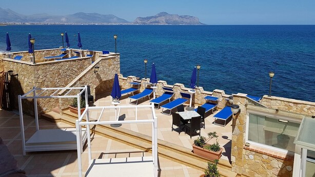 A rooftop terrace with blue lounge chairs and umbrellas overlooking the sea.