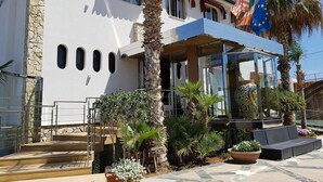 A hotel with a white facade, stone accents, and a covered outdoor seating area with potted plants.