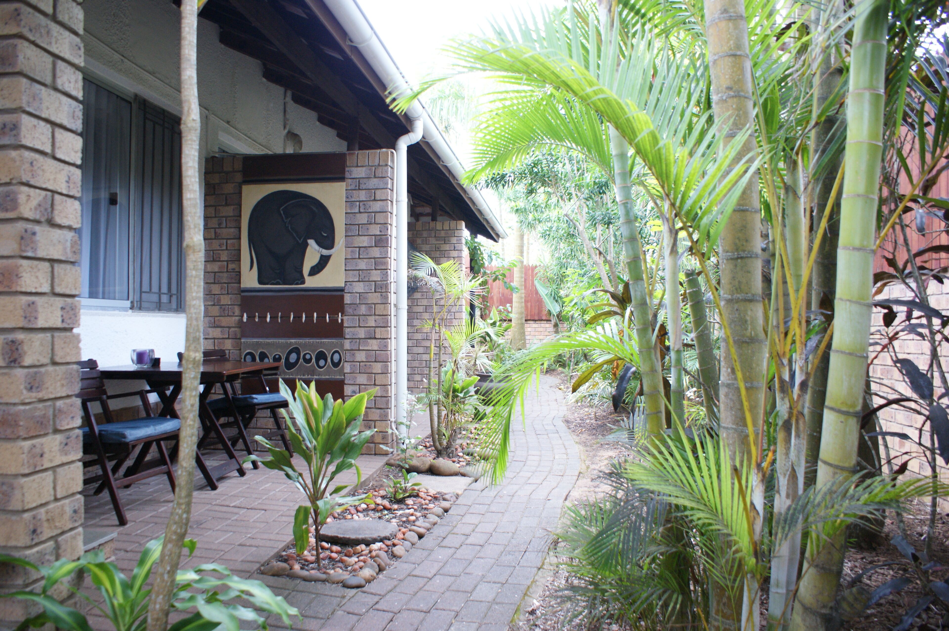 A brick building with a covered patio, outdoor seating, and a variety of plants.