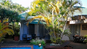 A swimming pool with a tiled deck, surrounded by palm trees and a covered patio area with outdoor furniture. - Bhangazi Lodge (St. Lucia)