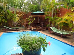 Une piscine entourée de meubles en bois et de plantes tropicales.