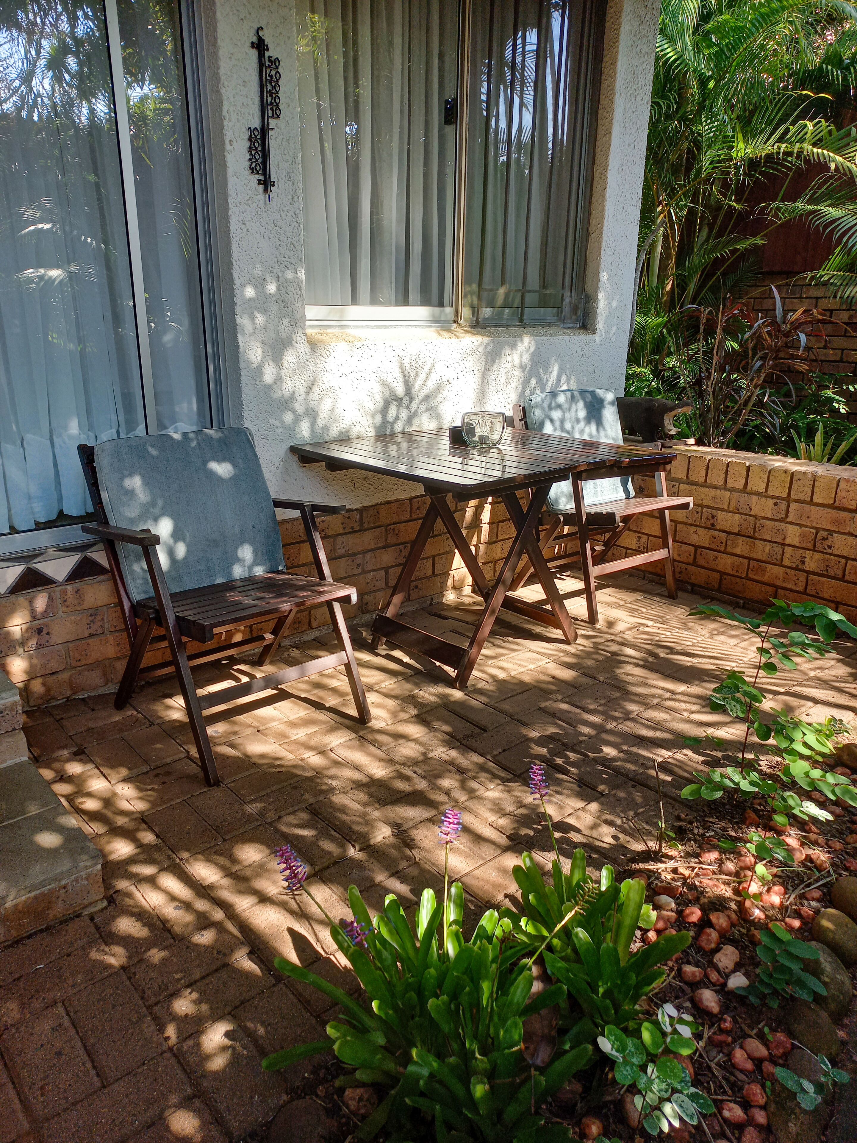 A patio with a table and chairs, surrounded by a brick wall and plants.
