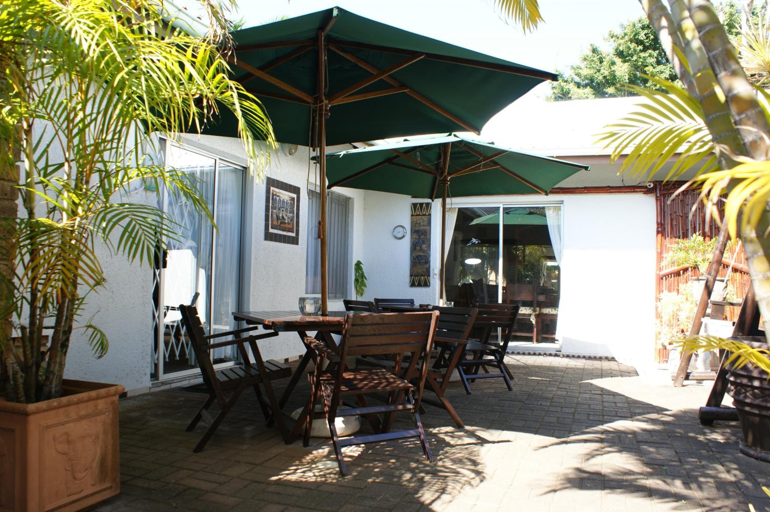 An outdoor patio with wooden furniture, green umbrellas, and potted plants.