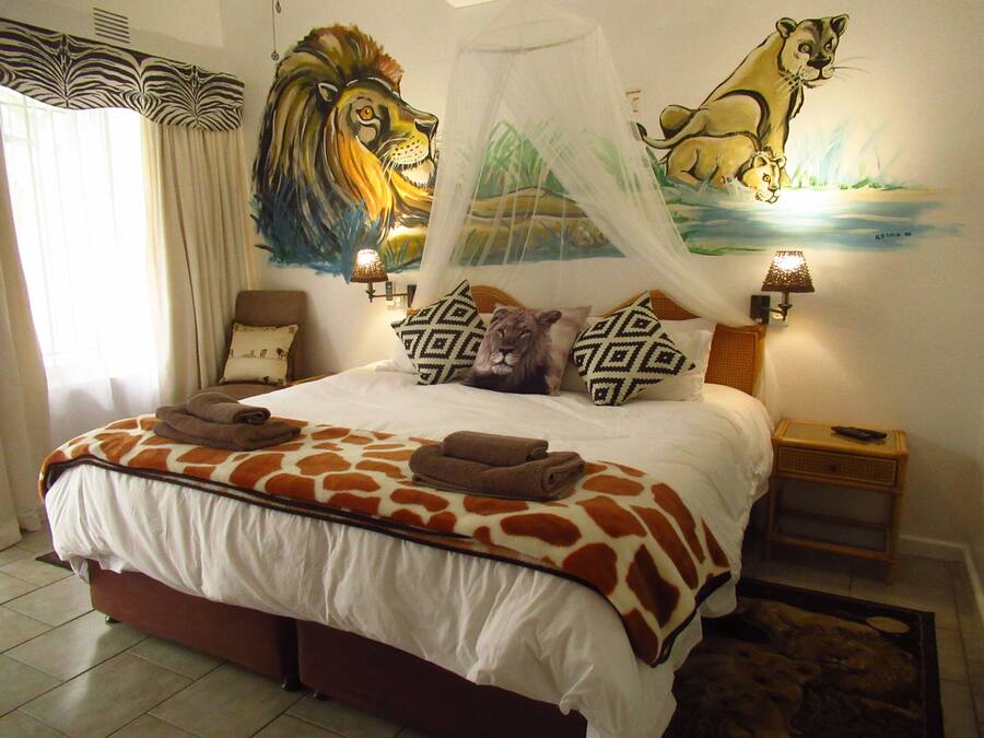 A bedroom with a bed, a lion mural, a zebra curtain, and a nightstand with a lamp.