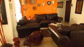 A living room with a brown leather sofa, a small red stool, and a decorative hippo sculpture on the floor.