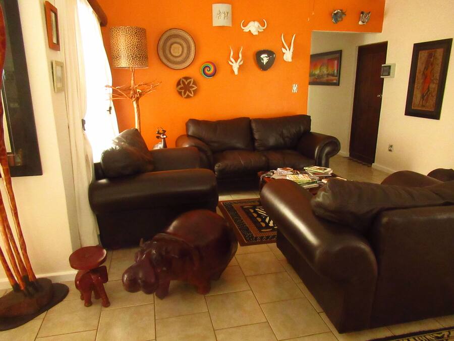 A living room with a brown leather sofa, a small red stool, and a decorative hippo sculpture on the floor.