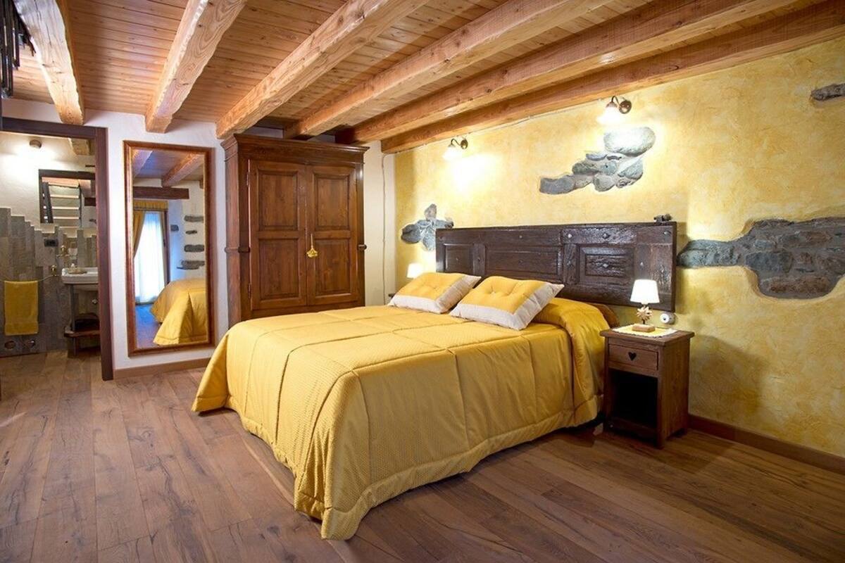 Un dormitorio con techo de madera, una cama con ropa de cama amarilla, una mesita de noche y una decoración de pared de piedra.