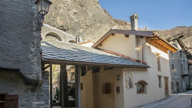 A traditional stone building with a sloped roof, a wooden door, and a small balcony. - La cor de Jeremie (Montjovet)