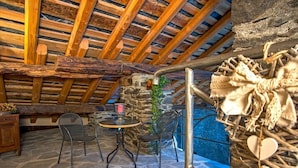 A rustic stone interior with a wooden ceiling, a stone wall, and a small table with chairs. - La cor de Jeremie (Montjovet)
