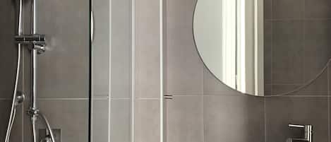 A modern bathroom with a glass-enclosed shower, a round mirror, and a black sink.