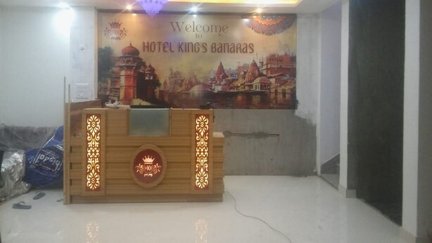 Una recepción con un mural de un paisaje urbano y un cartel de bienvenida del Hotel King's Banaras.