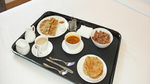 Una bandeja con diversos alimentos para el desayuno, incluyendo tortitas, sopa, café y frijoles, sobre una mesa blanca.