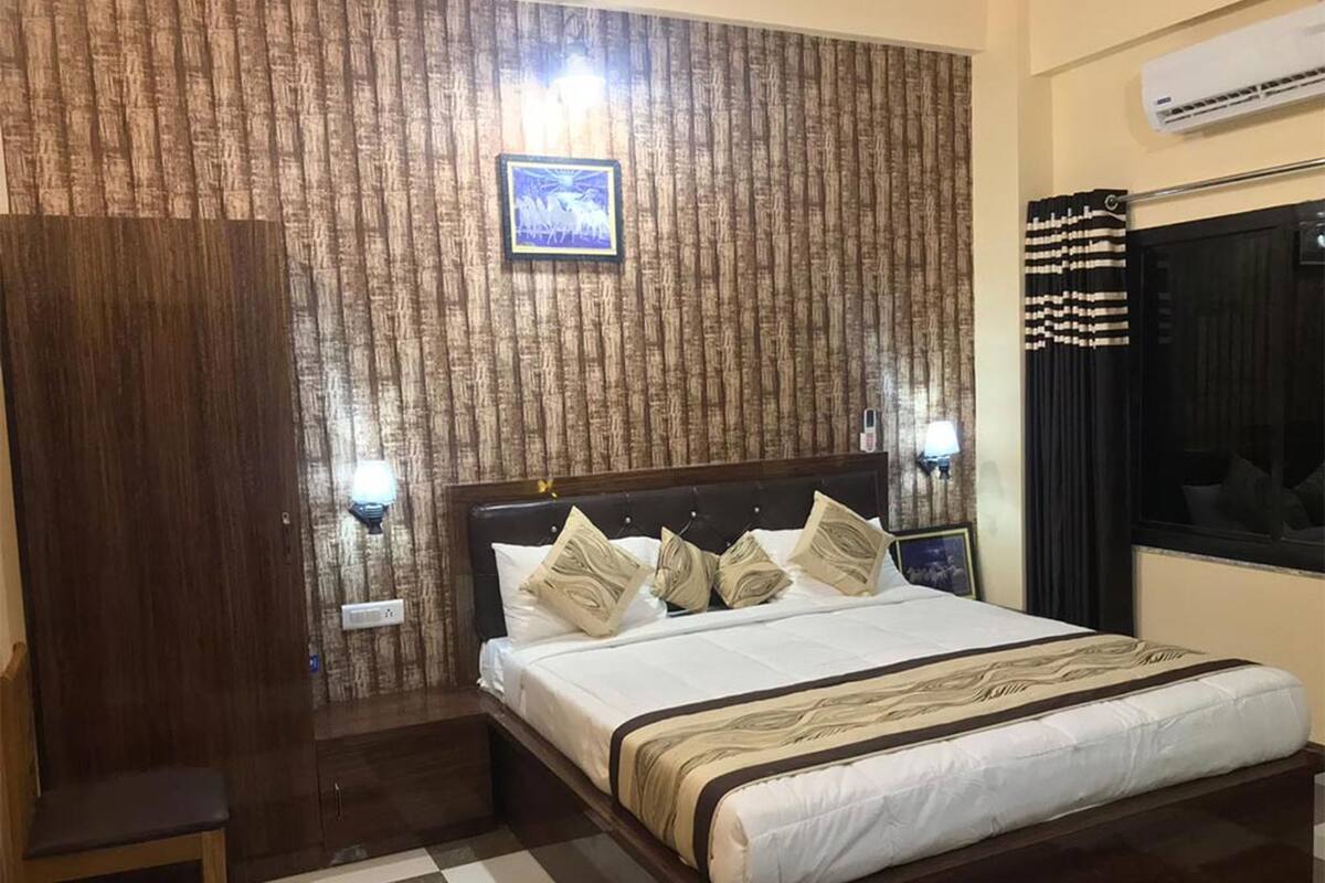 A hotel room with a large bed, a wooden wardrobe, a checkered floor, and a wall-mounted air conditioner.