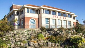 Un bâtiment à deux étages dont la façade porte l’inscription « PAVILLON », avec un socle en pierre et un toit plat.