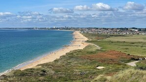 Un paysage côtier avec une plage, des champs couverts d’herbe et une ville située au loin.