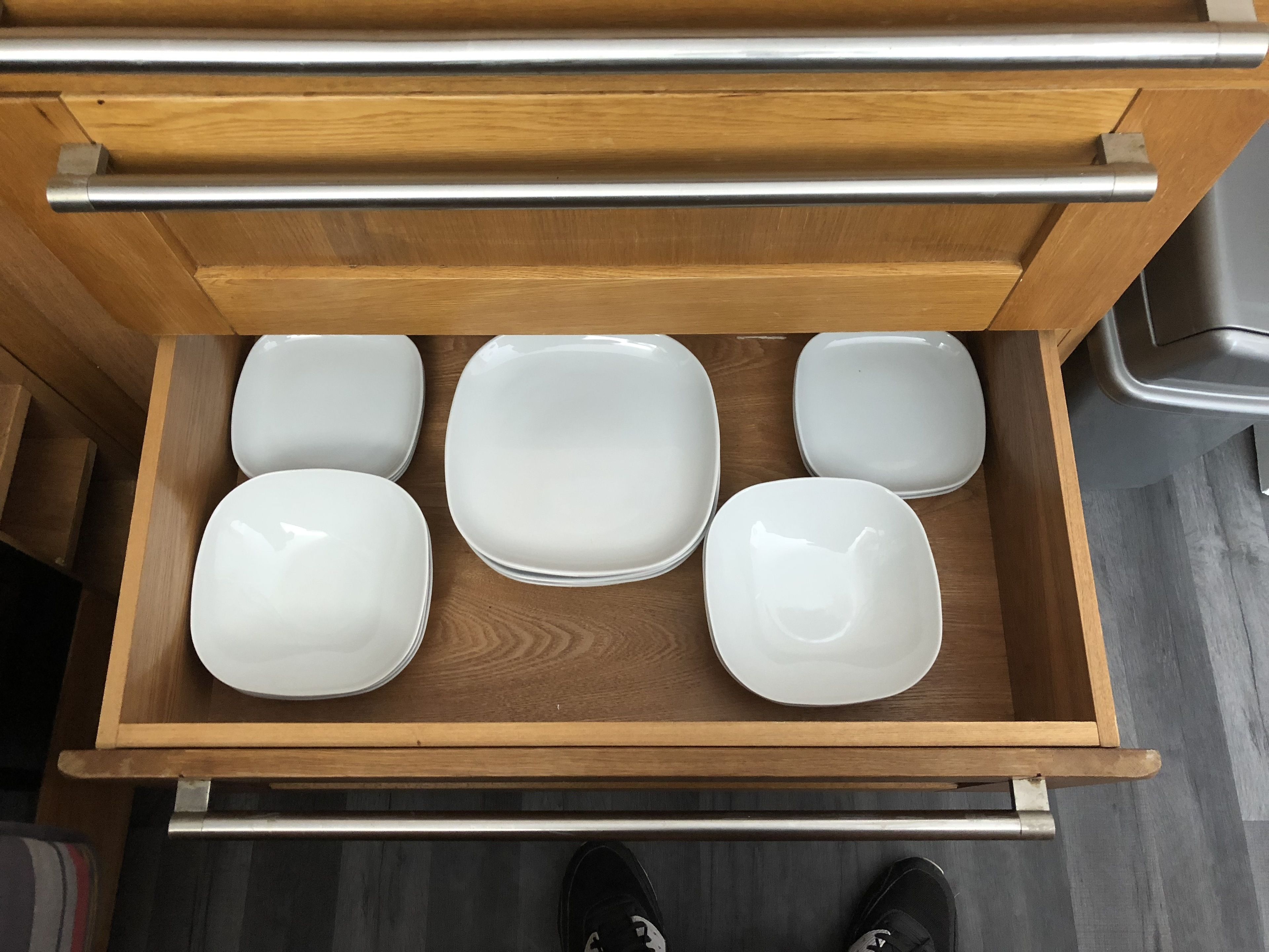 A drawer with five white plates and a metal handle.