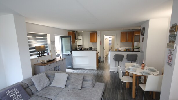 Un appartement moderne avec un canapé gris, une table à manger dressée pour quatre personnes et une cuisine en arrière-plan.