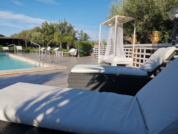 A poolside area with lounge chairs, a pergola with a canopy, and a pool.