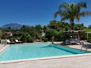 A pool with lounge chairs, a pergola, and a view of a mountain.