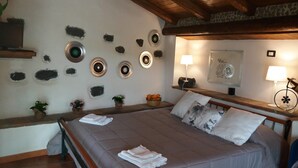 A bedroom with a bed, pillows, a bedside table, a lamp, a wall-mounted air conditioner, and decorative plates on the wall. - La Fattoria dei Nonni Resort dell'Etna (Paterno)